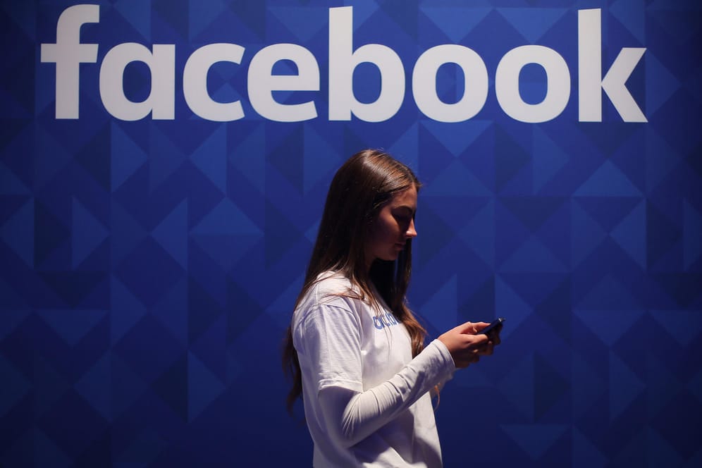 Eine Frau steht mit ihrem Smartphone unter dem Facebook-Schriftzug: Facebook bringt seine Dating-Funktion nach einer monatelangen Verzögerung wegen Datenschutz-Bedenken nun auch in Europa an den Start.
