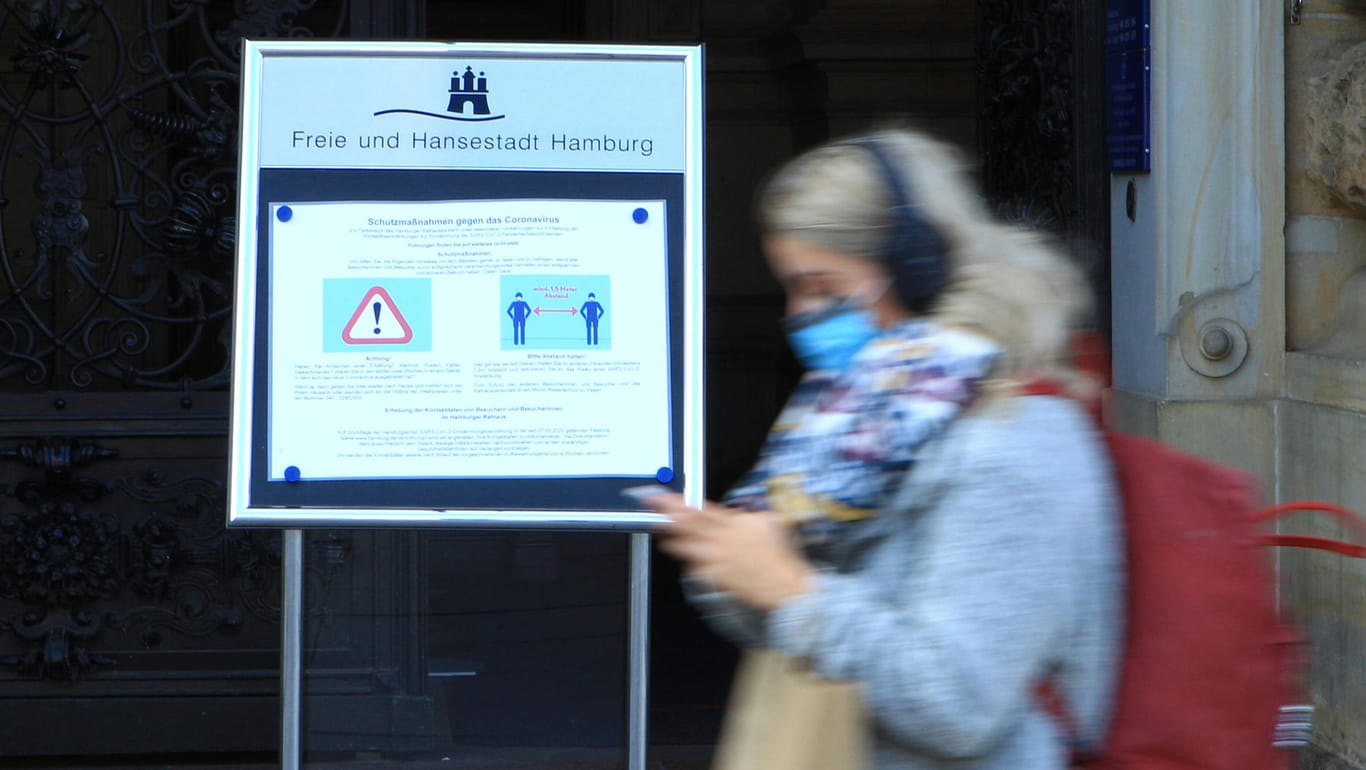 Eine Frau mit einer Mund-Nasen-Maske geht an einem Schild am Eingang des Rathauses in Hamburg vorbei (Archivbild): In der Hansestadt haben offenbar Corona-Infizierte vermehrt längeren Kontakt mit anderen Menschen.
