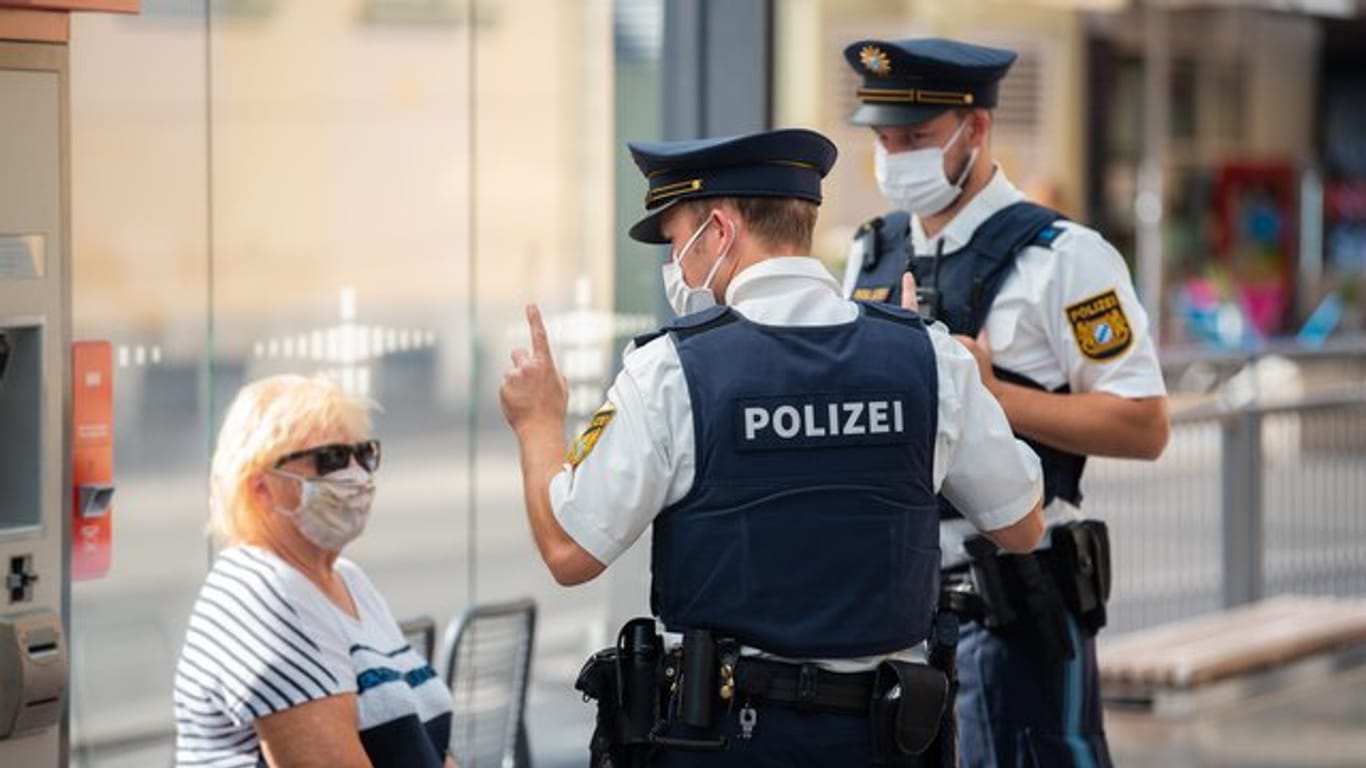 Zwei Polizisten nehmen an einer Tram-Haltestelle in Würzburg von einer Frau nach einem Verstoß gegen die Maskenpflicht im öffentlichen Nahverkehr die Personalien auf.
