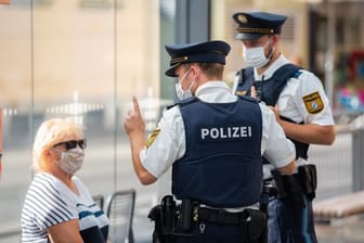 Zwei Polizisten nehmen an einer Tram-Haltestelle in Würzburg von einer Frau nach einem Verstoß gegen die Maskenpflicht im öffentlichen Nahverkehr die Personalien auf.