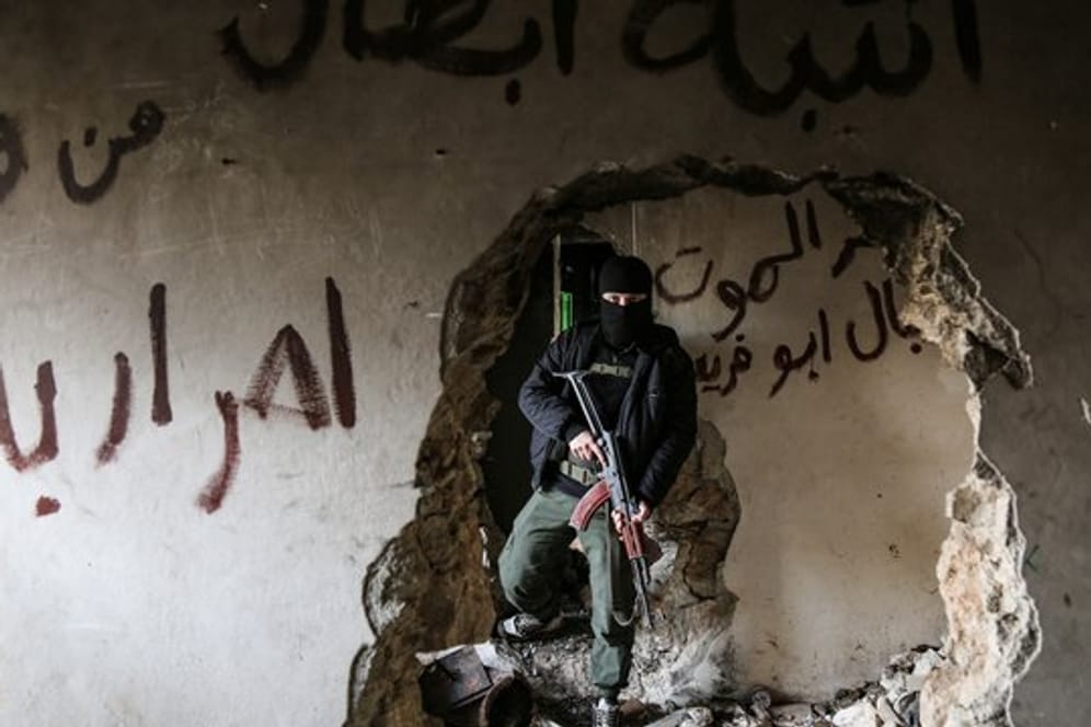 Ein bewaffneter Kämpfer der Miliz Haiat Tahrir al-Scham inspiziert ein beschädigtes Haus.