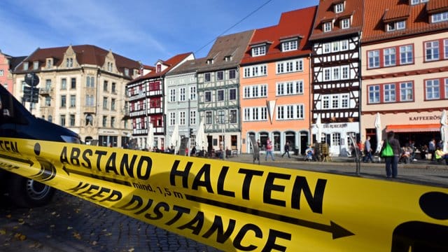 "Abstand halten!" in deutscher und englischer Sprache steht auf einem Flatterband am Domplatz in Erfurt (Archivbild): Auch Erfurt ist jetzt Corona-Risikogebiet.