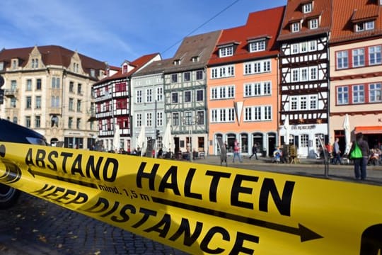 "Abstand halten!" in deutscher und englischer Sprache steht auf einem Flatterband am Domplatz in Erfurt (Archivbild): Auch Erfurt ist jetzt Corona-Risikogebiet.