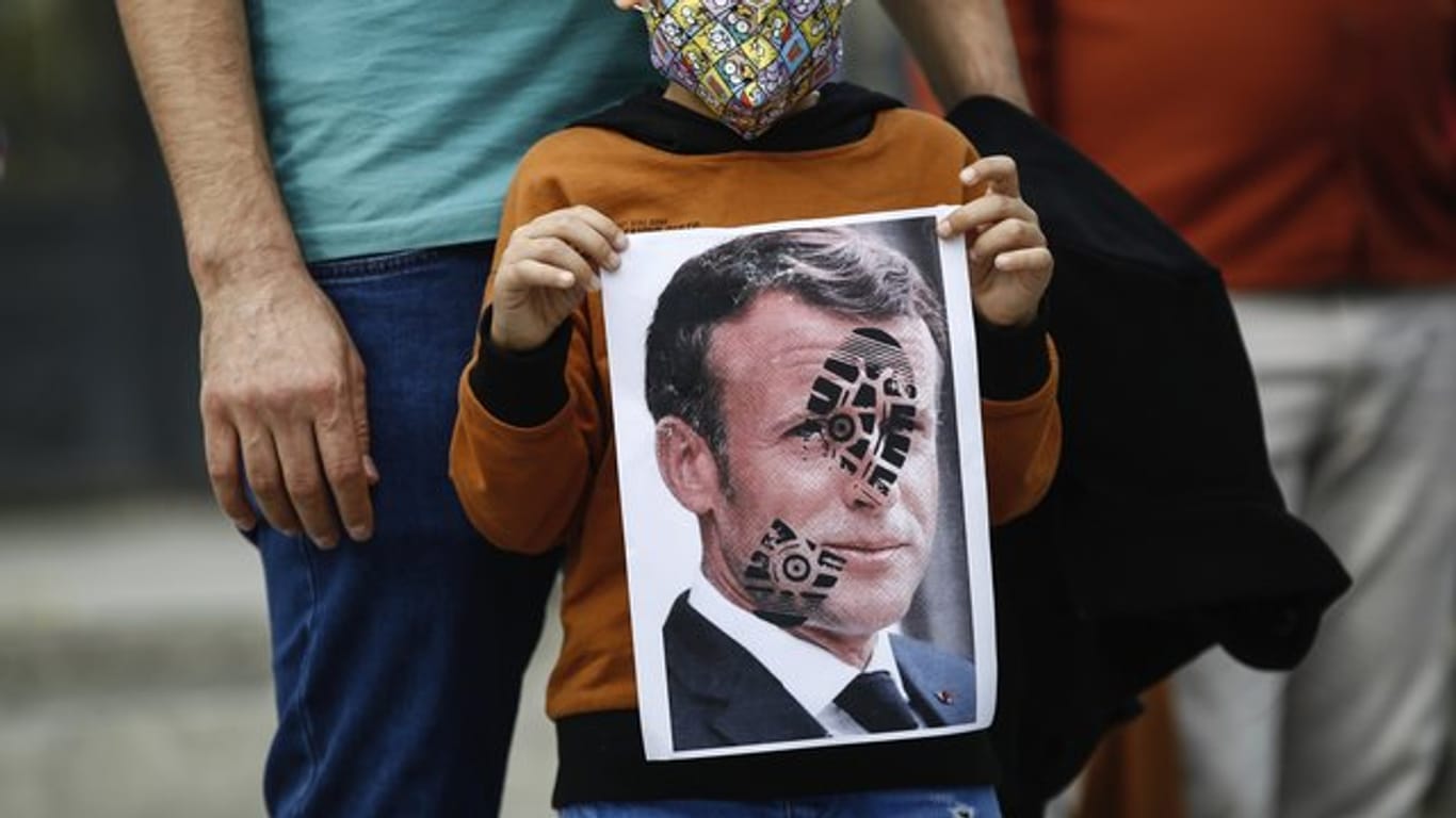 Ein Kind hält in Istanbul ein mit einem Schuhabdruck versehenes Foto von Emmanuel Macron in die Kamera: Der französische Präsident ist unter Beschuss.