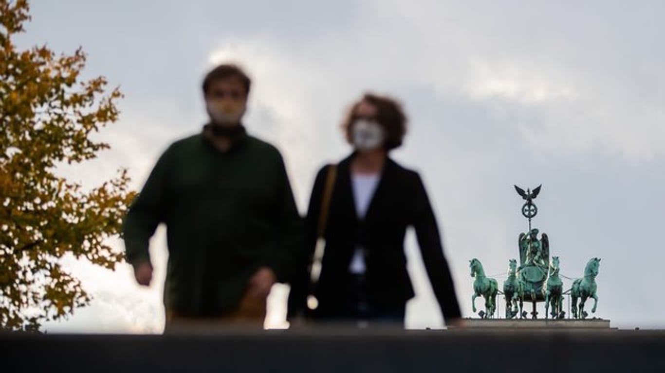 Ein Mann und eine Frau mit Mund-Nasen-Schutz vor der Quadriga des Brandenburger Tores in Berlin.