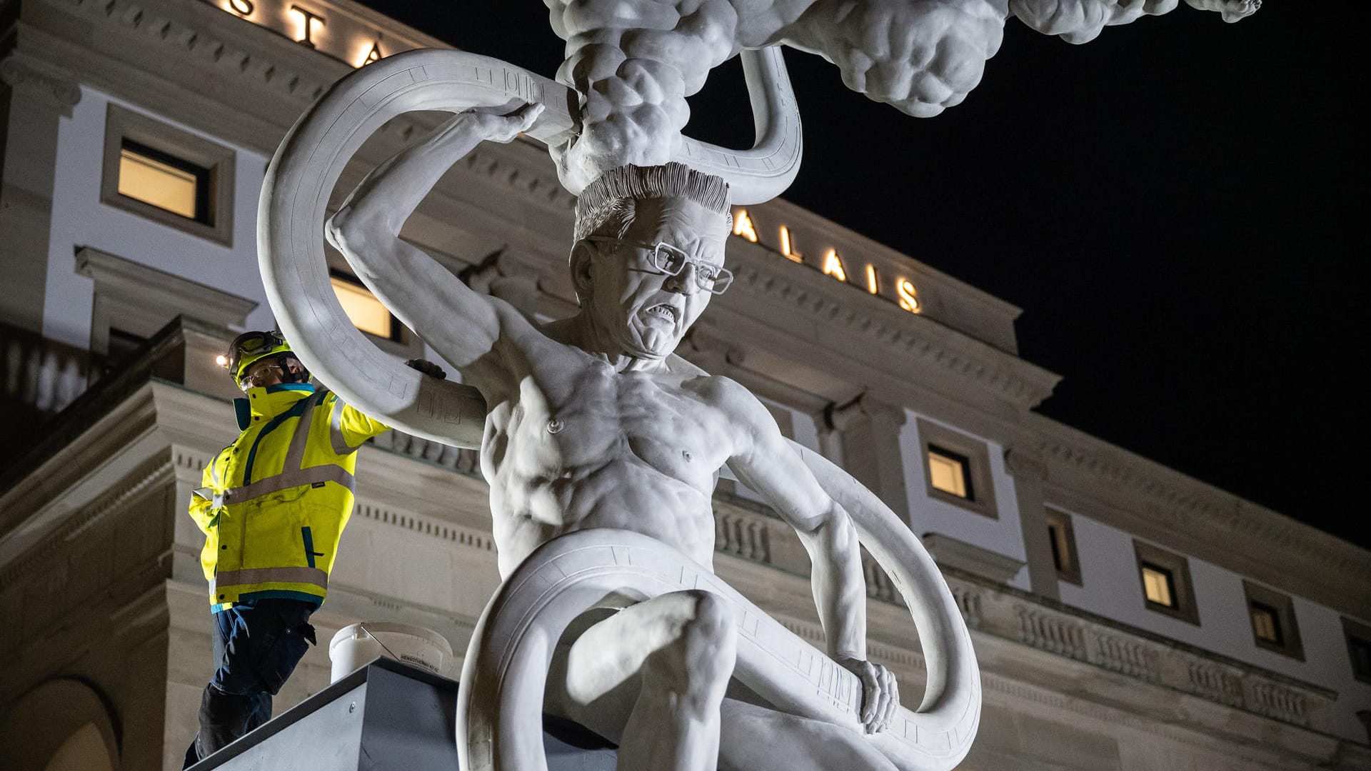 Ein Arbeiter steht neben der Skulptur des Künstlers Peter Lenk: Die Statue ist neun Meter hoch und zehn Tonnen schwer.