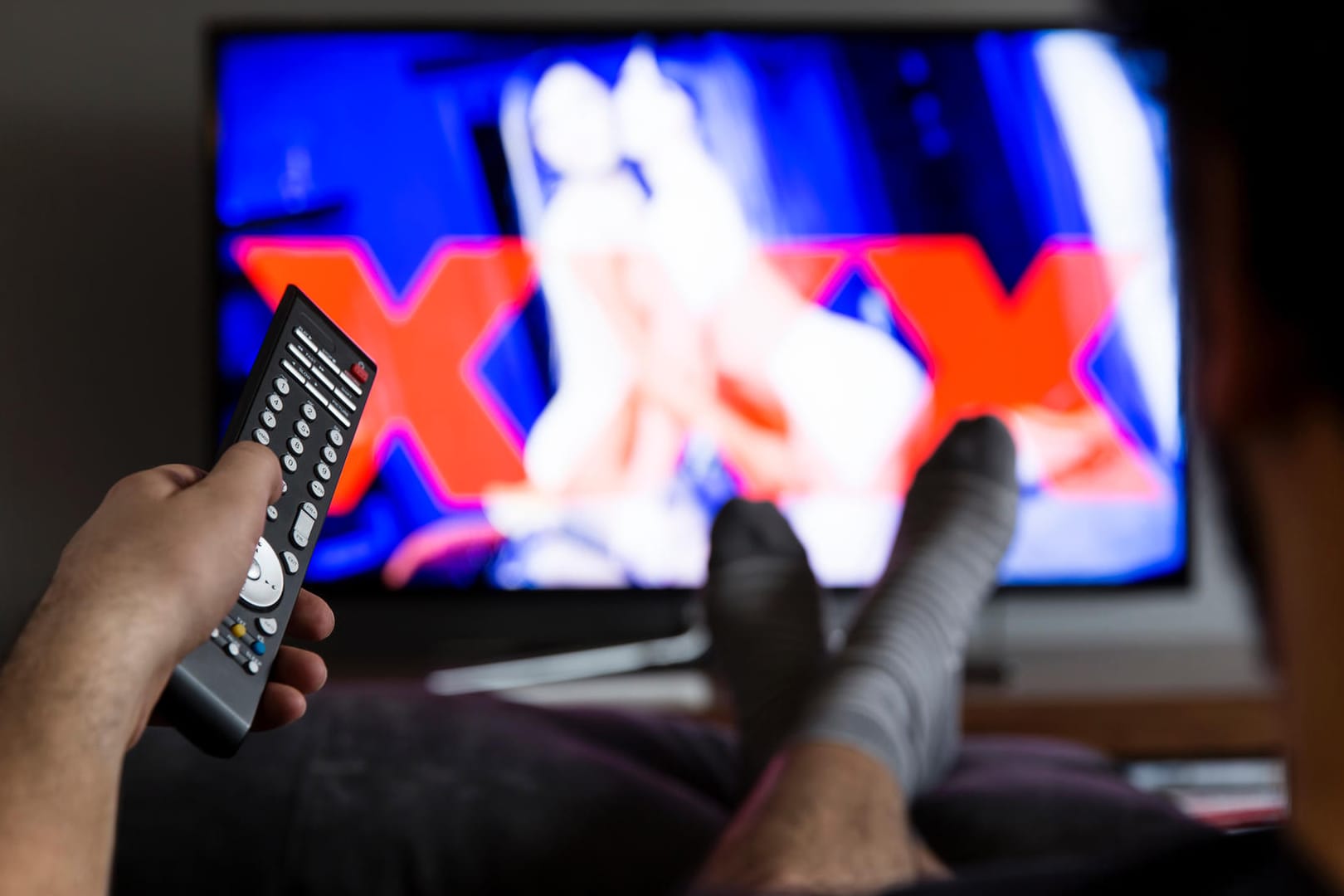 Ein Mann schaut einen Porno am Fernseher (Symbolbild): Die beliebte Seite xHamster lässt Freiwillige seine Inhalte und löschen.