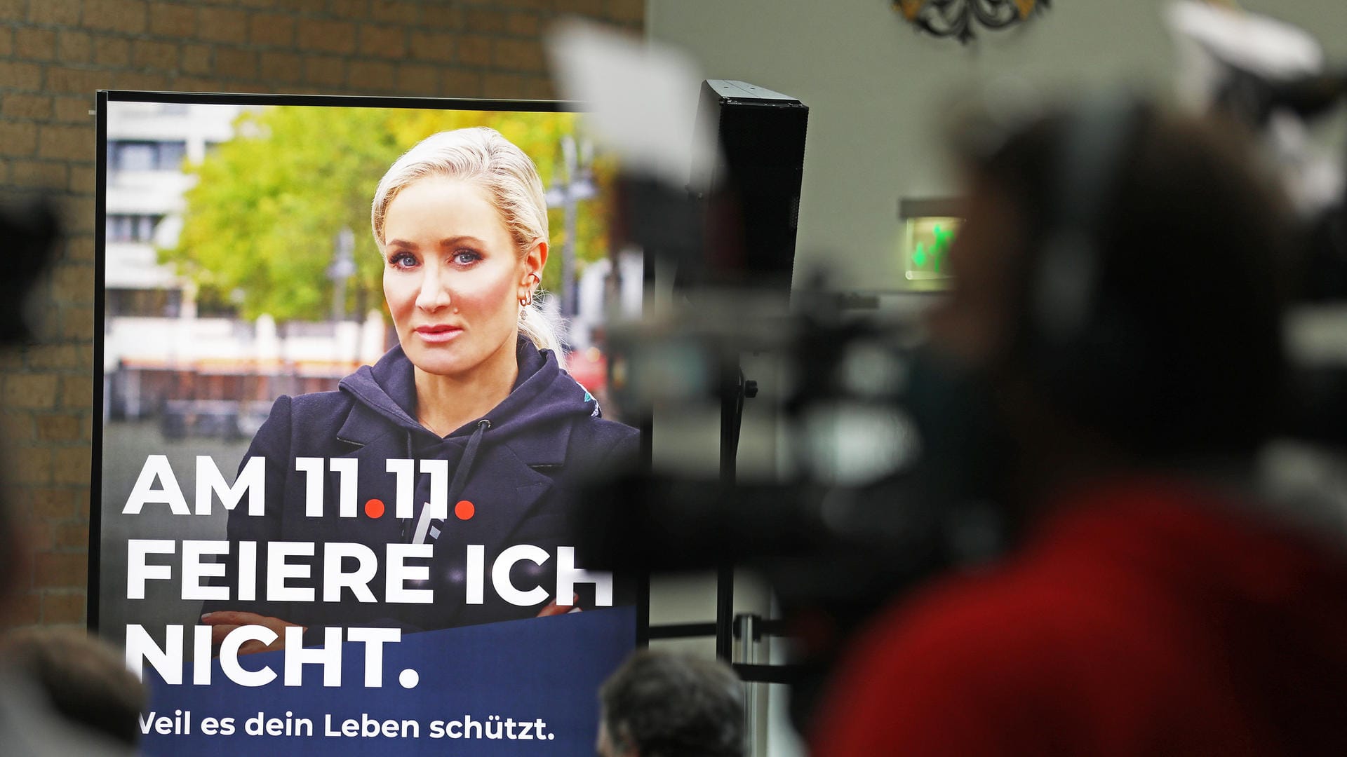 Hinter Kameraleuten ist ein Werbeplakat mit Schauspielerin und Moderatorin Janine Kunze und der Aufschrift: "Am 11.11. feiere ich nicht" zu sehen: Der Karnevalsauftakt in Köln muss dieses Jahr ausfallen.