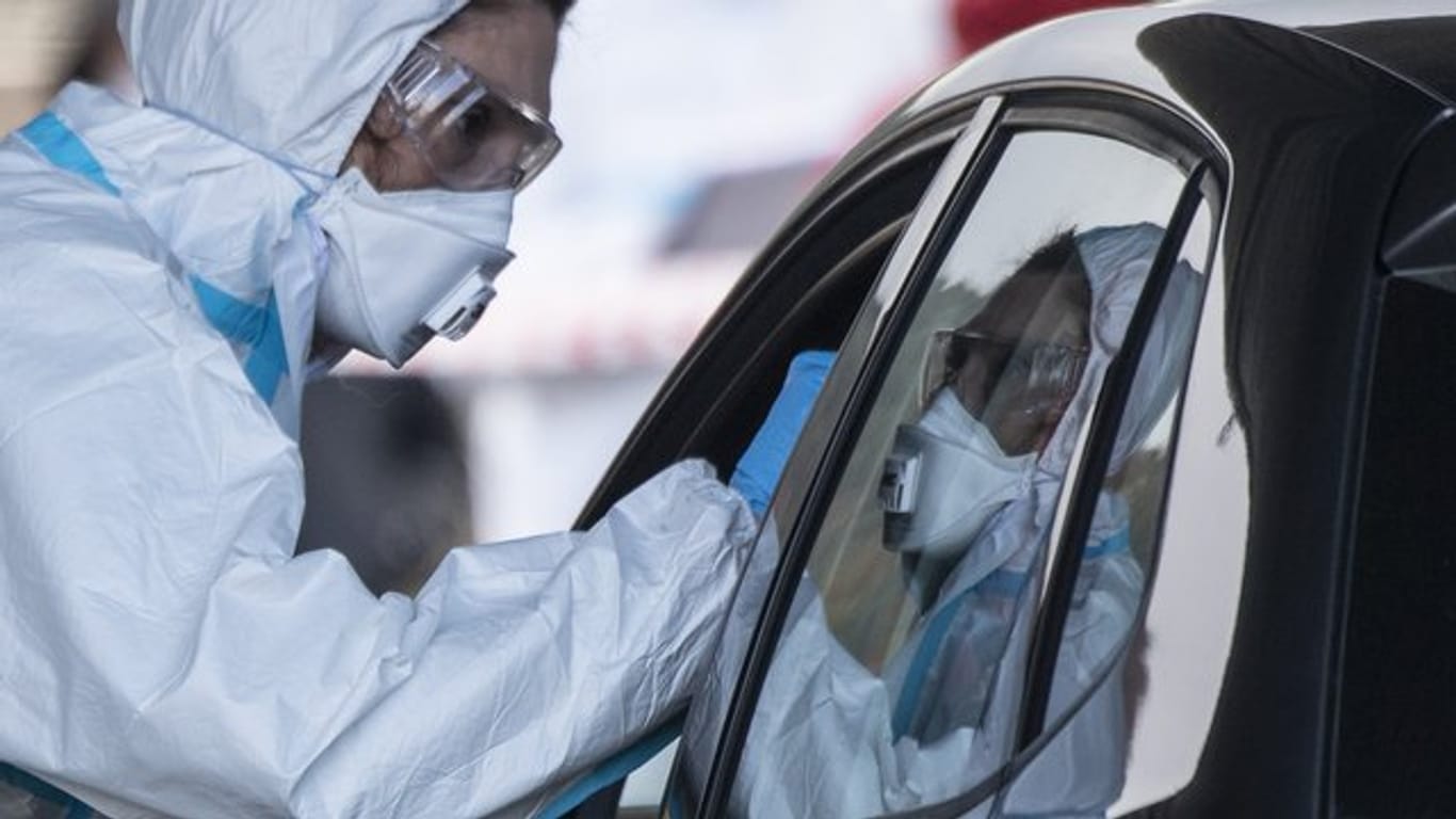 Ein Mitarbeiter eines Corona-Testzentrums auf dem Marburger Messegelände nimmt einen Abstrich von einem Autofahrer.