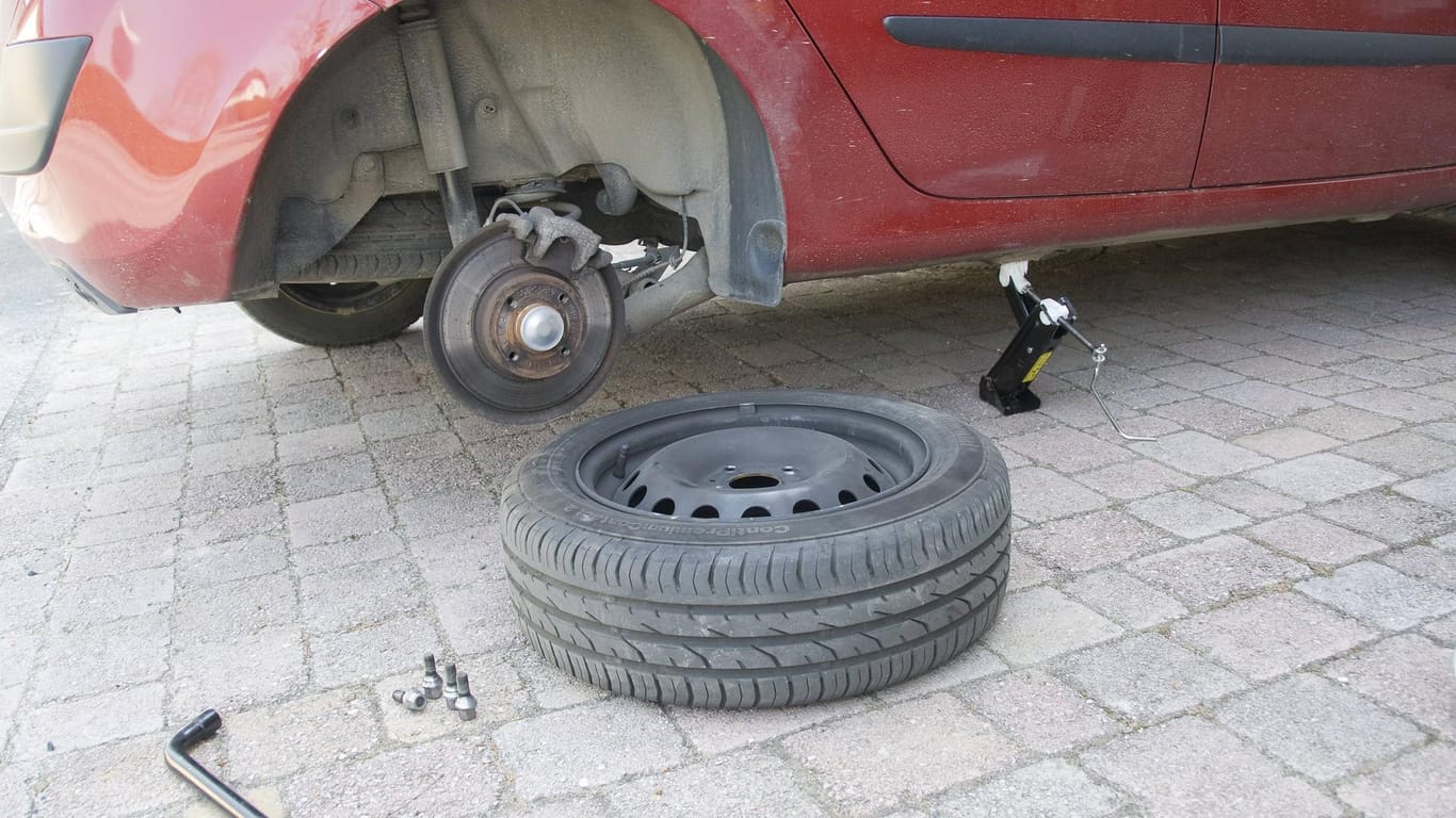 Ein abmontierter Autoreifen liegt vor einem aufgebockten Pkw (Symbolbild): Zwei komplette Radsätze wurden in einer Wolfsburger Tiefgarage gestohlen.