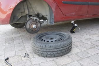 Ein abmontierter Autoreifen liegt vor einem aufgebockten Pkw (Symbolbild): Zwei komplette Radsätze wurden in einer Wolfsburger Tiefgarage gestohlen.
