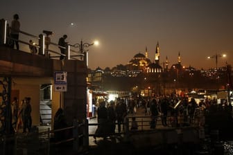 Menschen schlendern vor der Kulisse der Süleymaniye-Moschee am Ufer des Bosporus entlang.