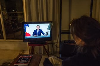Eine Frau verfolgt in Paris die TV-Ansprache von Staatspräsident Emmanuel Macron.