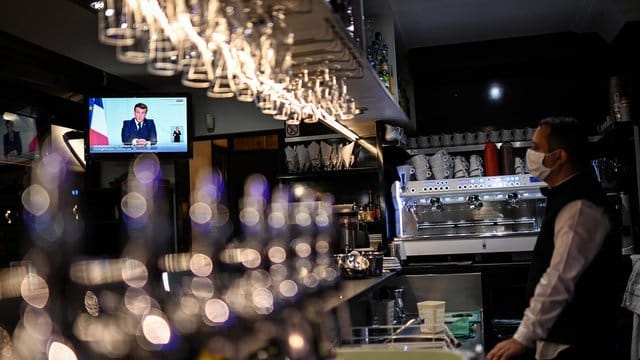 Ein Barkeeper schaut sich die Fernsehansprache von Präsident Macron in einem Café in Marseille an. Ein Barkeeper schaut sich die Fernsehansprache von Präsident Macron in einem Café in Marseille an.