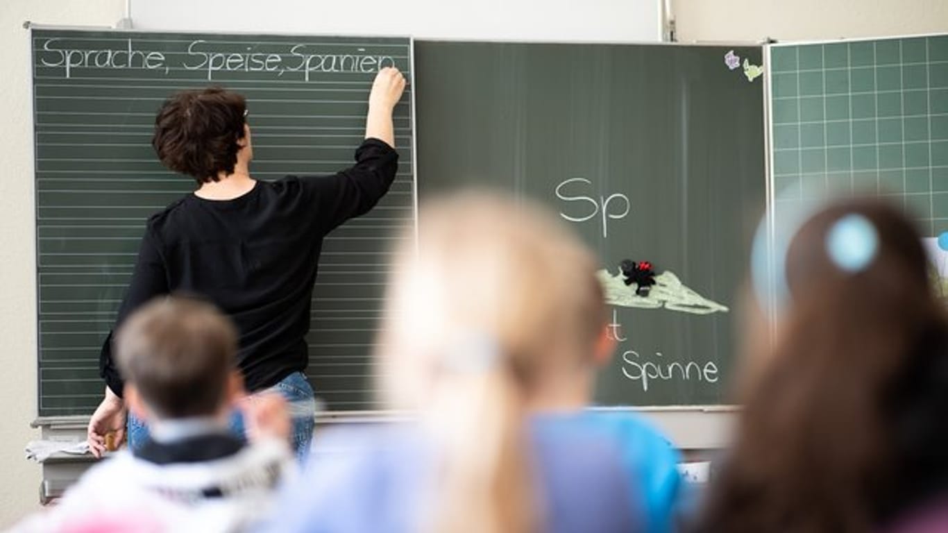 Eine Lehrerin schreibt in einer Schule an die Tafel (Symbolbild): Nach den Herbstferien gelten in Schulen und Kitas in Erfurt strengere Maßnahmen gegen das Coronavirus.