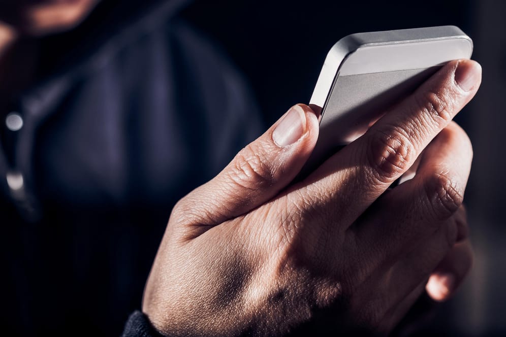 Ein Mann hält ein iPhone in der Hand (Symbolbild): Apple warnt vor Betrugsnachrichten an iPhone-Nutzer.