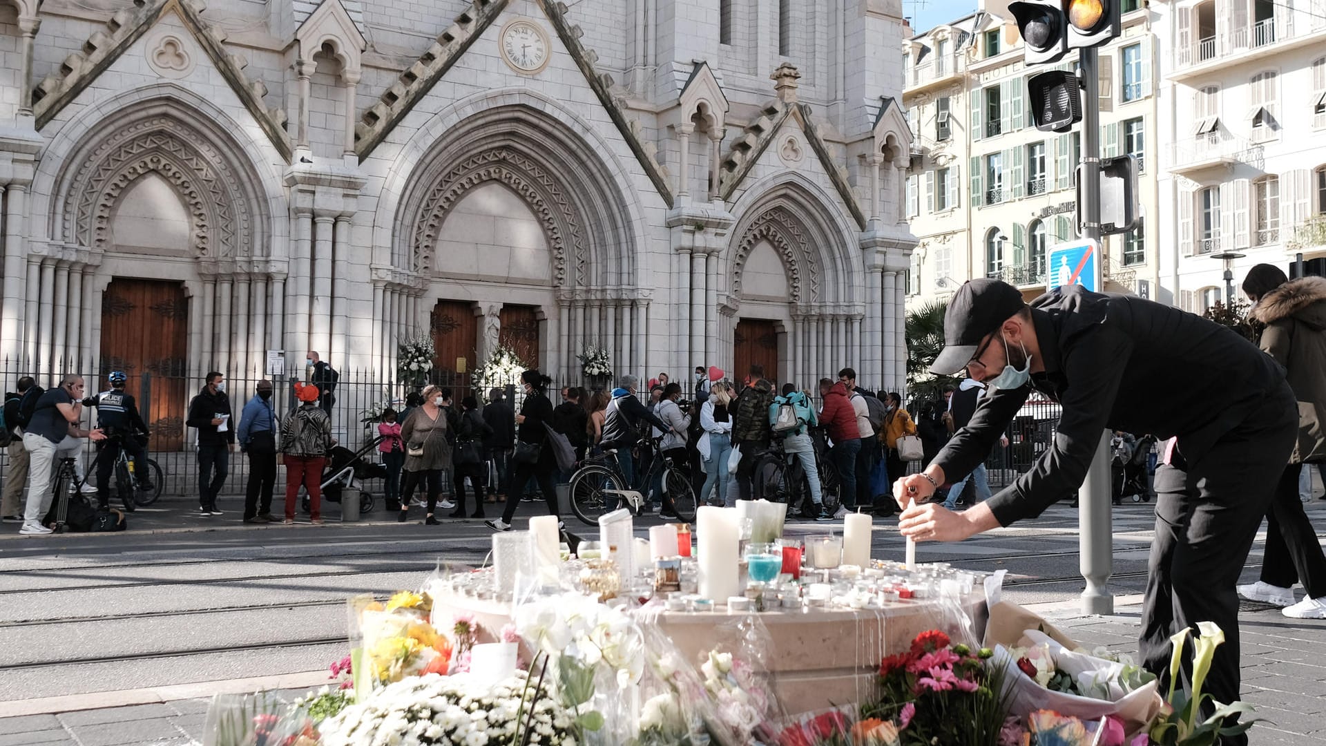 Frankreich, Nizza: Ein Mann zündet vor der Notre-Dame-Basilika zwischen Blumen eine Kerze an.