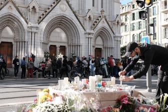 Frankreich, Nizza: Ein Mann zündet vor der Notre-Dame-Basilika zwischen Blumen eine Kerze an.