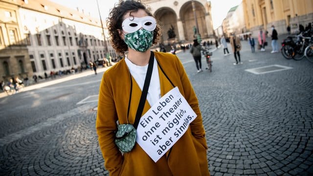 Auf einem Schild steht "Ein Leben ohne Theater ist möglich, aber sinnlos": Eine Mitarbeiterin der Kammerspiele bei einer Menschenkette.