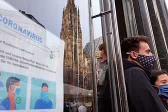 Zwei Personen, die Mund-Nasen-Schutz tragen, stehen in Wien neben einem Hinweisschild für das korrekte Tragen der Mund-Nasen-Bedeckung.