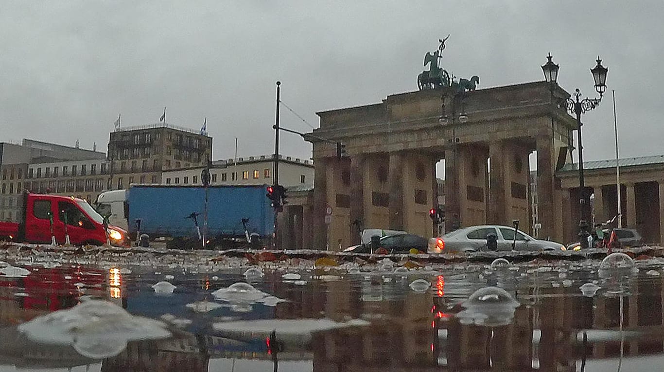 Berlin: Regentropfen sorgen für große Blasen auf einer Pfütze am Brandenburger Tor.