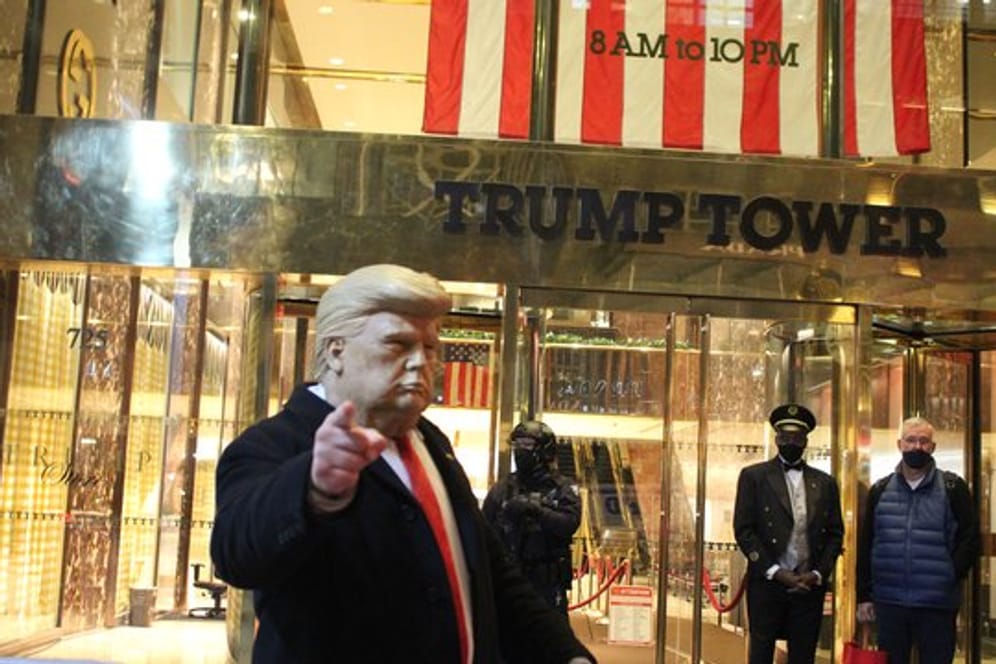 Ein Mann mit einer Trump-Maske in der Hand gestikuliert vor dem Trump Tower, der von einem Polizisten einer Spezialeinheit des NYPD auf der 5th Avenue in Manhattan am Vorabend der Präsidentschaftswahlen gesichert wird.