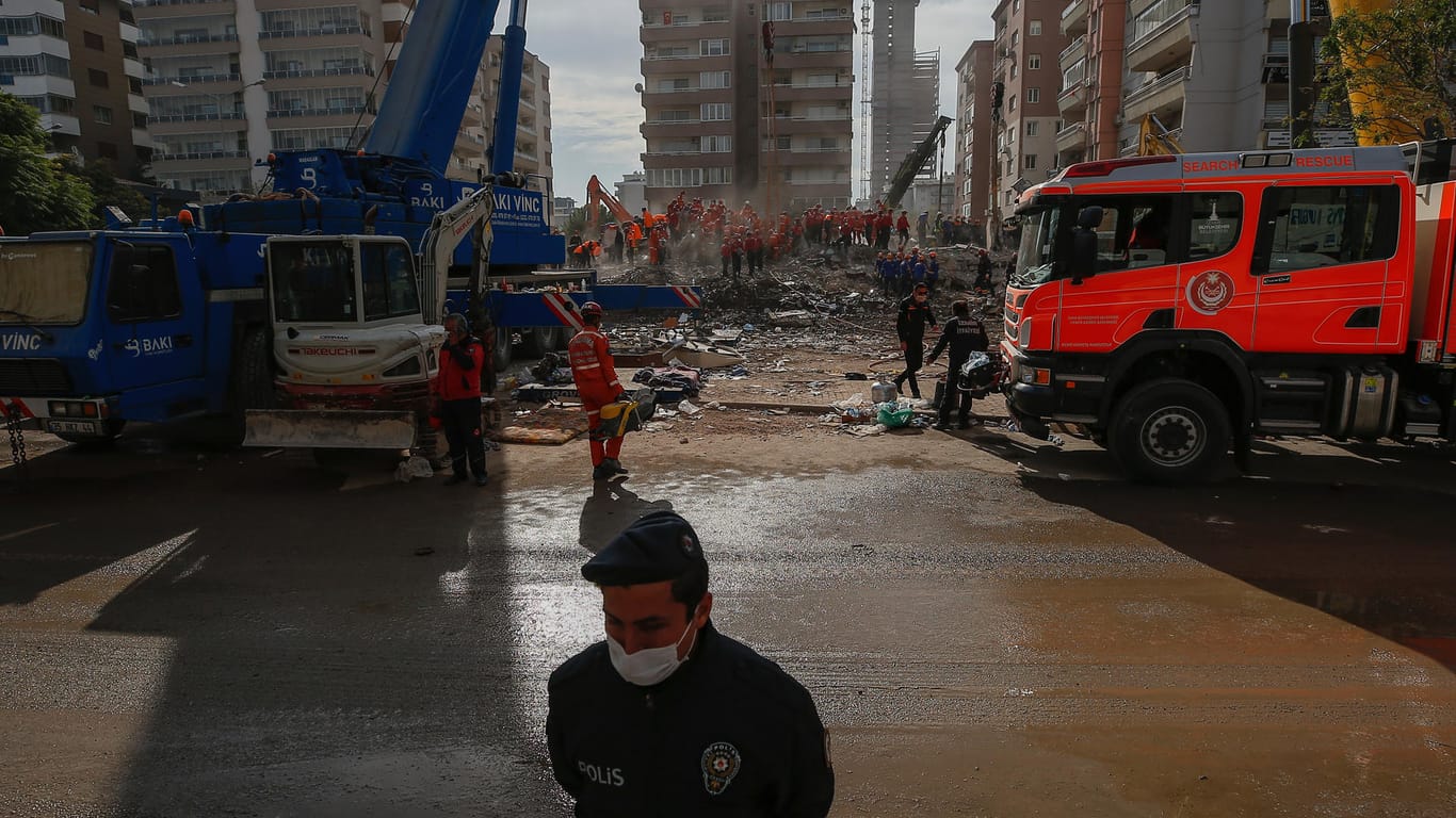 Türkei, Izmir: Ein Polizist steht Wache am Gelände auf dem Mitglieder von Rettungsdiensten in den Trümmern eines eingestürzten Gebäudes nach Überlebenden suchen.