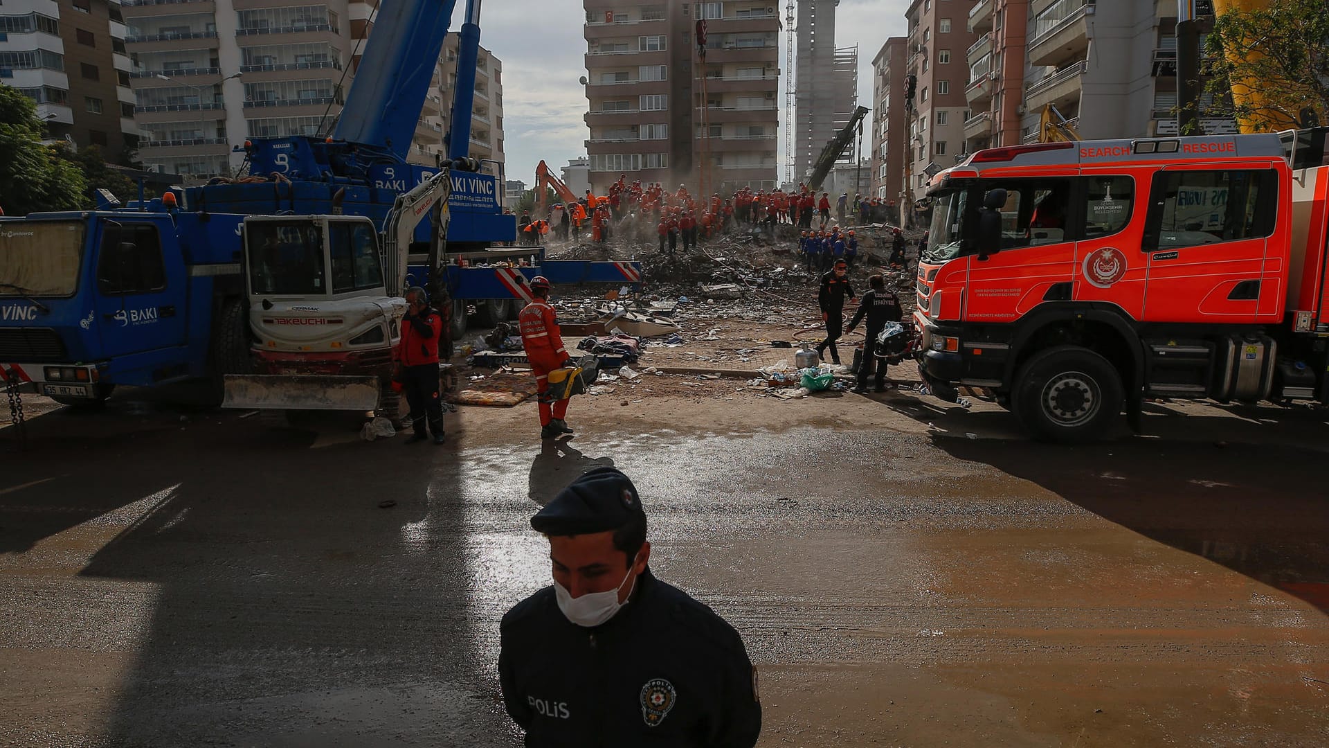 Türkei, Izmir: Ein Polizist steht Wache am Gelände auf dem Mitglieder von Rettungsdiensten in den Trümmern eines eingestürzten Gebäudes nach Überlebenden suchen.