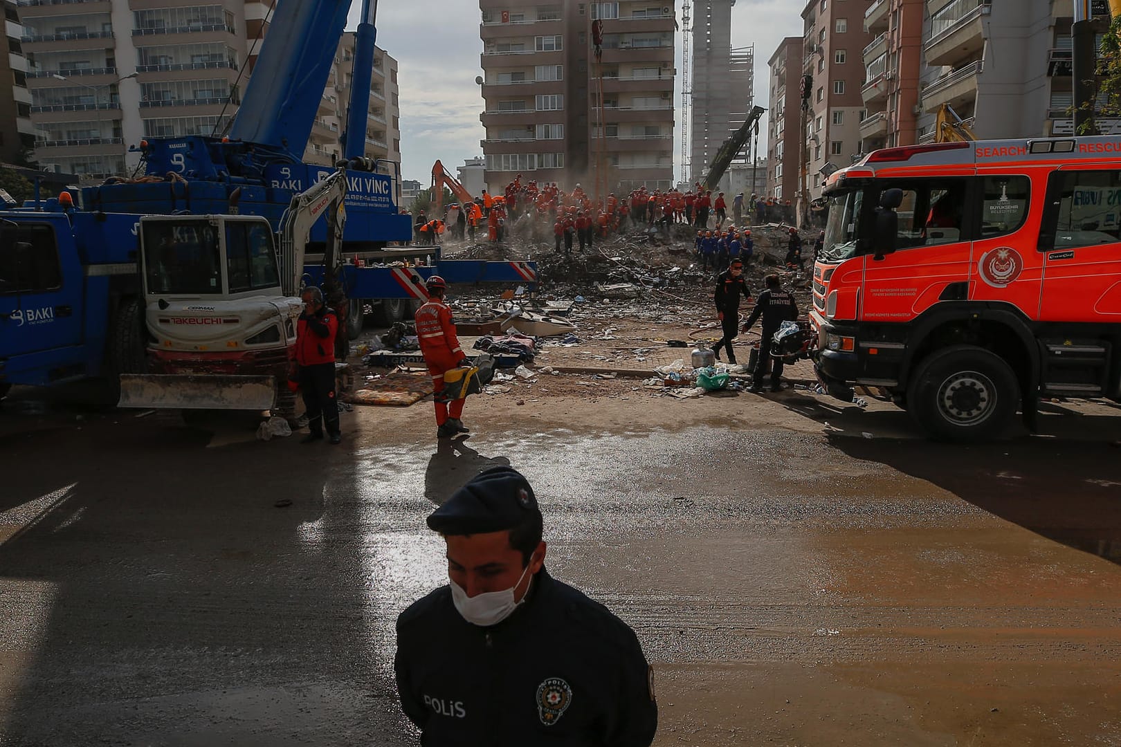 Türkei, Izmir: Ein Polizist steht Wache am Gelände auf dem Mitglieder von Rettungsdiensten in den Trümmern eines eingestürzten Gebäudes nach Überlebenden suchen.