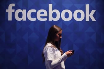 Eine Frau steht mit ihrem Smartphone unter dem Facebook-Schriftzug.