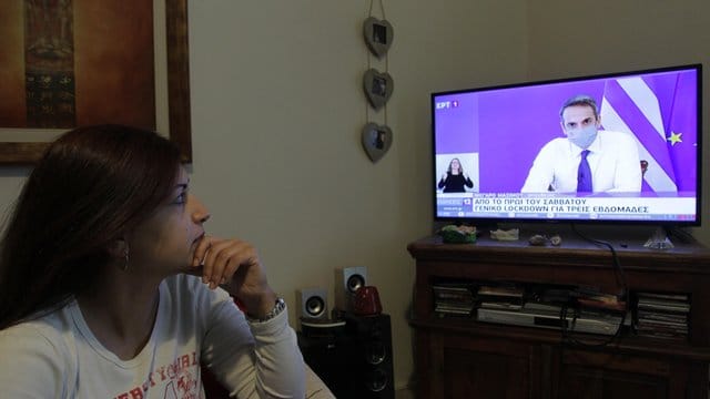 Eine Frau verfolgt die TV-Ansprache von Griechenlands Premierminister Mitsotakis. Eine Frau verfolgt die TV-Ansprache von Griechenlands Premierminister Mitsotakis.