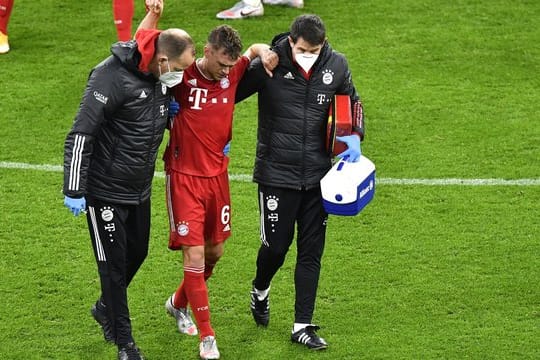 Bayerns Joshua Kimmich geht nach einer ärztlichen Behandlung gestützt von den Betreuern vom Platz.