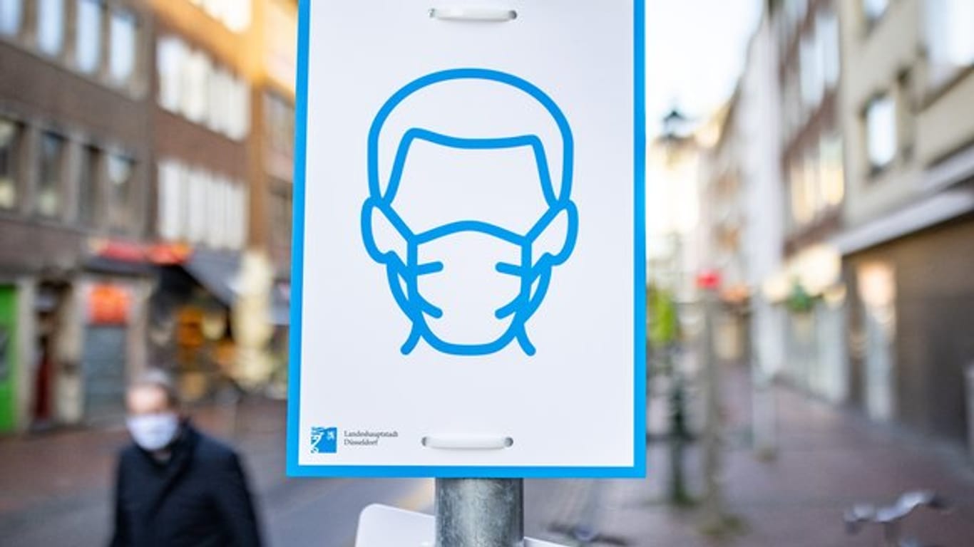 Ein Schild mit dem Symbol für Maskenpflicht an einem Straßenschild in der Innenstadt von Düsseldorf.