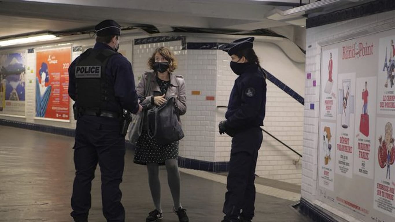In einer U-Bahn-Station in Paris kontrollieren zwei Polizisten eine Pendlerin.