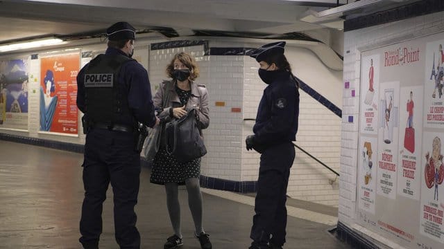 In einer U-Bahn-Station in Paris kontrollieren zwei Polizisten eine Pendlerin. In einer U-Bahn-Station in Paris kontrollieren zwei Polizisten eine Pendlerin.