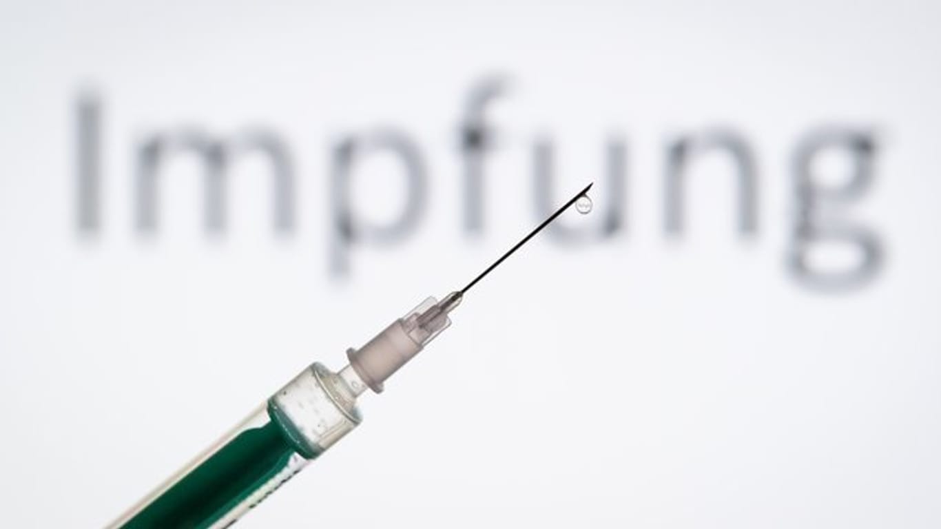 Eine Spritze wird vor den Schriftzug "Impfung" gehalten