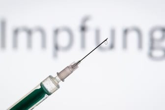 Eine Spritze wird vor den Schriftzug "Impfung" gehalten