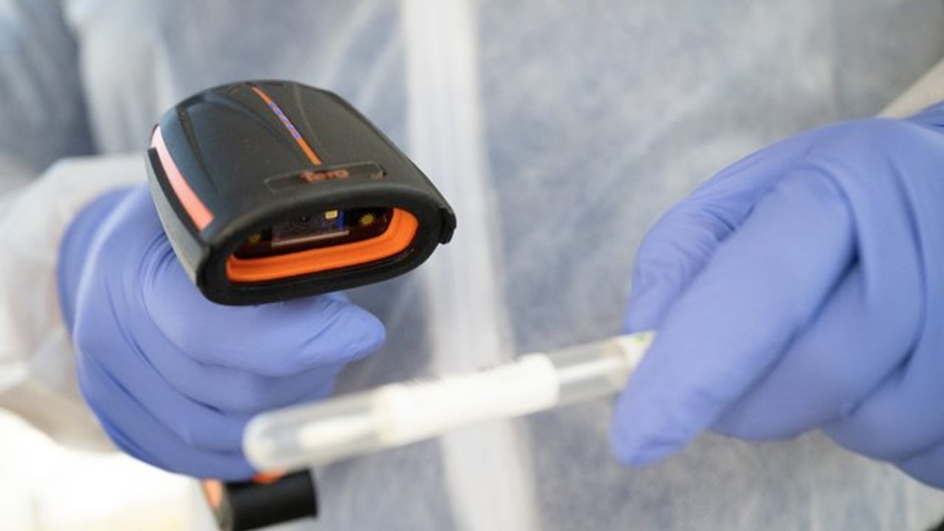 Ein Arzt in Schutzkleidung scannt ein Teststäbchen in einer mobilen Corona-Teststation.