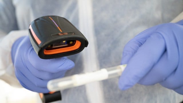 Ein Arzt in Schutzkleidung scannt ein Teststäbchen in einer mobilen Corona-Teststation. Ein Arzt in Schutzkleidung scannt ein Teststäbchen in einer mobilen Corona-Teststation.