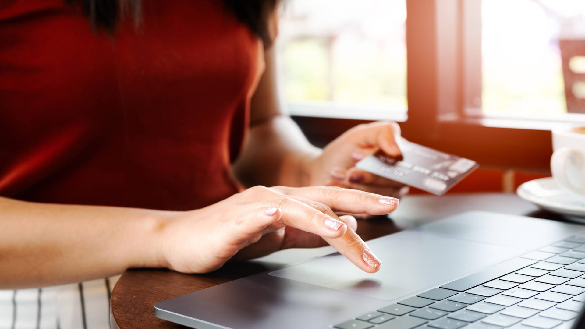 Eine Frau hält ihre Kreditkarte am Laptop in der Hand (Symbolbild): Die Polizei Wolfsburg warnt vor Betrügern beim Online-Einkauf.