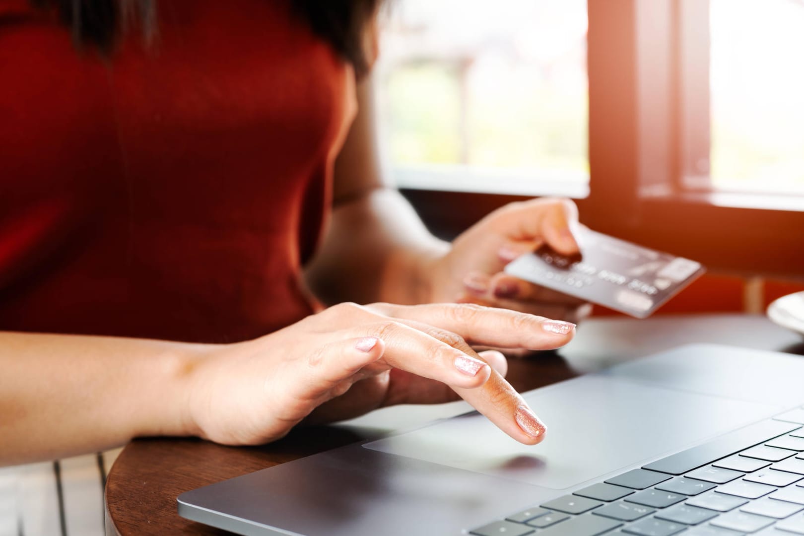 Eine Frau hält ihre Kreditkarte am Laptop in der Hand (Symbolbild): Die Polizei Wolfsburg warnt vor Betrügern beim Online-Einkauf.