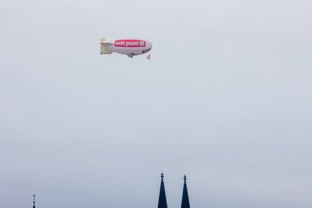 Ein Zeppelin mit der Aufschrift "bliev zohuss" (Bleib zu Hause) der Roten Funken fliegt über den Kölner Dom.