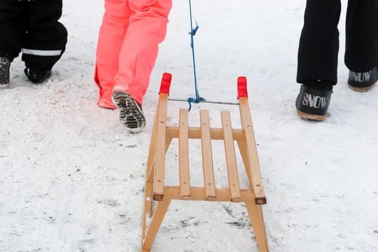 Winterurlauber gehen mit einem Schlitten zu einer Rodelbahn.