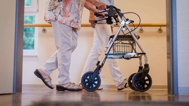 Eine Pflegekraft geht in einem Pflegeheim mit einer älteren Dame über einen Korridor.