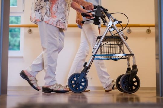 Eine Pflegekraft geht in einem Pflegeheim mit einer älteren Dame über einen Korridor.
