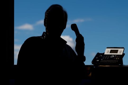 Ein Mann hält ein Telefon (Symbolbild): Betrüger haben viel Geld von einer 85-Jährigen gezockt.