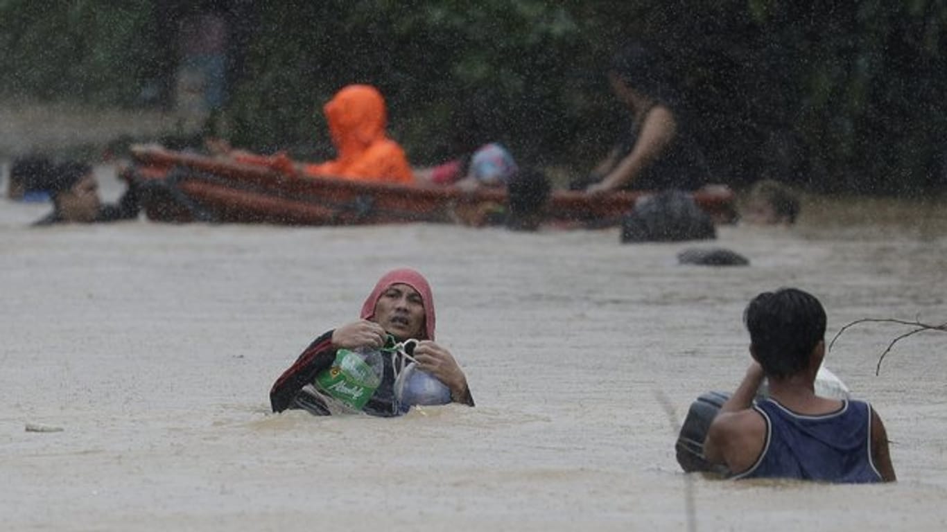Ein Mann in Marikina benutzt Plastikbehälter, um sich beim Überqueren einer überfluteten Straße über Wasser zu halten.