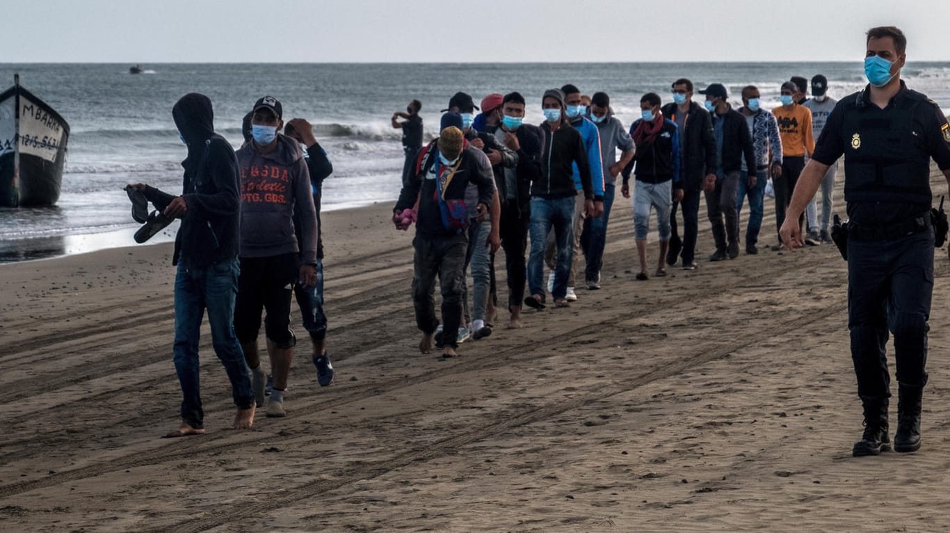 Migranten aus Marokko und ein spanischer Polizist auf Gran Canaria: Seit Jahresbeginn erreichten knapp 14.000 Migranten die Inselgruppe vor Westafrika.