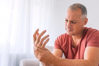 Mann schaut schmerzverkrampft auf seine Hand: Rheuma und weitere Erkrankungen können auch zu einer Osteoporose führen.