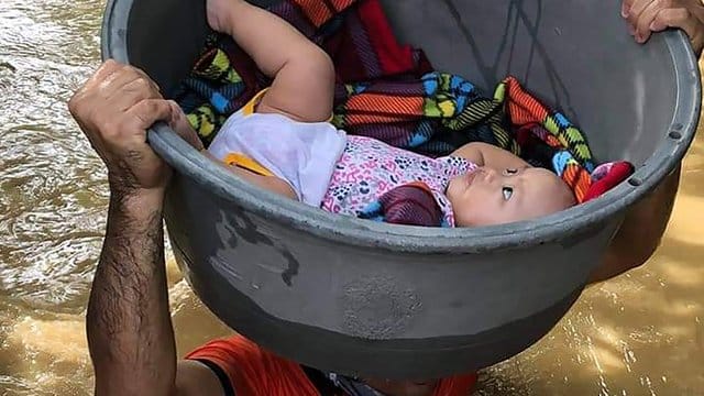 Ein Mann trägt ein Baby in einem Plastikbehälter. Ein Mann trägt ein Baby in einem Plastikbehälter.